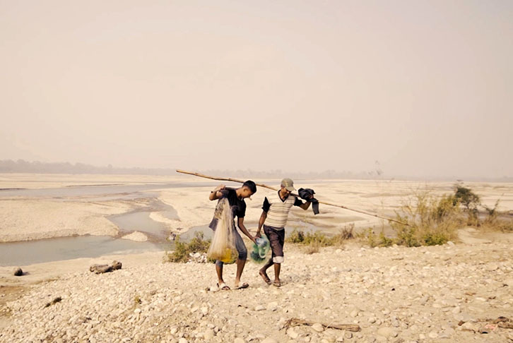Nepali fishers walk up from a dried out lake with their catch from the day