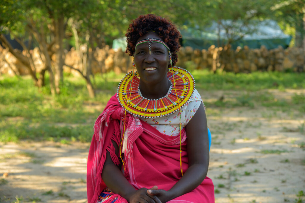 a Kenyan woman - participant n Alert's peacebuilding and climate adaptation project - wearing traditional clothes, sitted on a chair, smiling at the camera
